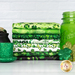 A stack of fabric with a black pot with gold joins, a sparkly hat, shamrocks, and a glass jar.