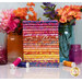 A stack of the batik fabrics included in the Sunset collection, with mason jars and flowers and thread.