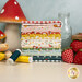 A stack of the fabrics included in the Serendipity 2 FQ Bundle, with mushrooms and strawberries and a milk bottle and tulips and thread.