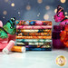 A stack of the fabrics included in the Flight of Beauty FQ bundle, with flowers and butterflies and a jar and thread.