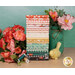 A stack of the fabrics included in the Sunsetridge collection, with flowers and a jar and a bird and thread.