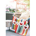 A colorful quilt with heart designs drapes over a chair beside a small log table in a garden setting.