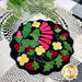 A top down shot of the completed Strawberry Zinger wool mat kit in black and bright colors, staged on a lace doily.