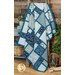 A patchwork quilt in blue tones draped over a wooden ladder in a rustic setting with coordinating decor. 