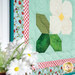 A stylized close up on the lower left corner of the project, showing fabric print and color details. Coordinating flowers peek into frame.
