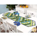 The completed Greased Lightning Table Runner in green, blue, and yellow fabrics from the Limoncello collection, staged on a white table with coordinating cloth napkins, florals, and summer decor.