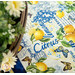 A super close shot of the white wordy citrus print on the placemat, demonstrating fabric and binding details. White florals can be seen peeking into frame from the left side.