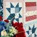 Close-up of a colorful quilt featuring star patterns in blue, red, and floral fabrics with flowers in the foreground.