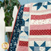 Patchwork quilt draped over a white fence, featuring red, white, and blue star patterns.