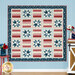 A patriotic quilt featuring star and striped patterns in red, white, and blue, displayed against a blue wall next to coordinating decor. 