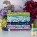 A stack of the fabrics included in the Seaside Garden collection, with flowers and jars and thread.