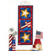The finished Foundation Paper Piecing Series 3 July project colored in patriotic colors, hung on a golden craft hanger on a white paneled wall above coordinating patriotic decor set on a wooden tabletop.
