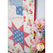 Close-up of a colorful quilt featuring floral and star patterns, beside pink flowers in a vase.