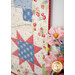 A colorful quilt featuring floral patterns and a star design hanging on a wall next to pink flowers in a vase.