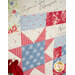 Close-up of a quilt featuring floral and star patterns, inscribed with inspirational text, with roses in the foreground.
