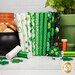 A stack of the fabrics included in the Paddy's Parade FQ bundle, with a pot of gold and a jar and a pot with a plant and four leaf clovers and thread.