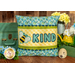 The finished June pillow wrap kit, a yellow wrap with blue and green scalloped borders and an appliqué bee beside appliqué letters that read 