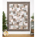 A patchwork quilt displayed on a wall, featuring nature inspired patterns in soft browns and blues.