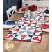 The completed Just a Sliver Tablerunner, colored in red, white, blue, and navy fabrics from the Grand Haven collection by Moda Fabrics, staged on a rustic wooden table and staged with coordinating napkins, four place settings, and red flowers in the center of the table.