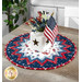 A round table mat featuring red, white, and blue patterns, holding a white vase with flowers and a small American flag.