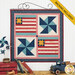 The completed July Pieceful Patchwork wall hanging, colored in cream, red, blue, and teal fabrics from the Americana collection by Lori Holt for Riley Blake Designs. The project is hung on a white paneled wall and staged with coordinating vintage americana decor.
