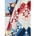A patriotic quilt featuring a geometrical design in red, white, and blue hanging next to coordinating decor, 