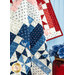 A patchwork patriotic quilt in red, white and blue, hanging against a light blue wall near a red vase with blue flowers