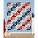 A geometric patchwork quilt in red, white, and blue featuring patriotic designs hanging on a wall
