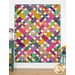 The completed Picnic Quilt colored in vibrant fabrics from the Wild Abandon collection, hung on a white paneled wall and staged with coordinating flowers and furniture.