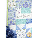 A stylized close up on the quilt, demonstrating fabric colors, prints, and panel details. Flowers peek into frame from the lower left corner.