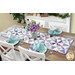 A dining table set with a colorful quilted table runner, floral vase, and neatly arranged place settings.