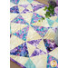 Colorful quilt featuring intricate geometric patterns in purple, teal, and cream, accented by plants.