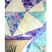 Close-up of a colorful quilt featuring geometric patterns in purples and blues, with hints of gold, next to a fork.