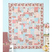 A colorful quilt featuring patchwork designs in pink, blue, and floral patterns, displayed on a wall.