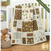 A patchwork quilt in the neutral brown and tan tones from the Into the Woodlands collection draped over a white crib, set with coordinating baby toys and decor. 