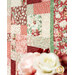 An angled shot of the patchwork edge of the quilt, demonstrating fabric, piecing, border, and stitching details. A blurred bouquet of flowers peeks into the bottom edge of the frame.