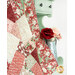 A close up shot of the quilt draped over a mint green armoire, showcasing the stitching and fabric designs. A metal pitcher holds a red and pink rose near the quilt.