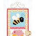 A close up on the top bee block of the project, hung on a golden craft hanger. The top of the honeypot block peeks into frame from the bottom.