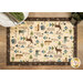 A top-down shot of a tan placemat with woodland animals and other outdoorsy motifs, with a brown border and staged on a wooden table with tableware peeking into frame from the top.