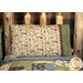 A shot of the Magic Pillowcase in tan and green, staged on a bed with a matching patchwork quilt in a cabin setting.