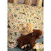 An angled shot of the Magic Pillowcase in tan and green, staged on a bed with a matching patchwork quilt and moose plushie in a cabin setting.