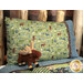 A full shot of the Magic Pillowcase in green, blue, and brown, staged on a bed with a matching patchwork quilt and moose plushie in a cabin setting.