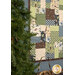 An angled shot of the quilt hung on a wall and staged next to a small tree and lantern that can be seen peeking into frame from the bottom.