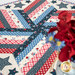 A closer look at the red, white, and blue topper, demonstrating fabric details and patchwork. Red and blue flowers peek into frame from the right side.