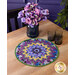 The completed Point of View Kaleidoscope Folded Star Table Topper colored in vibrant purple fabrics from the Pansy Perfection collection, staged on a wooden table with coordinating flowers and glass ware.