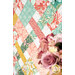 A stylized close up on the patchwork, showing fabric color and print details; coordinating roses peek into frame from the right side.
