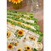 A close up on the four placemats, fanned out and staged with jars with handles, showing detail on the sunflower themed newsprint pattern and green leaf border fabric.