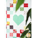 A shot of a patchwork heart framed by leaves in the foreground.