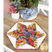 The completed 60 Degree Diamond Table Topper colored in bright yellow, red, pink, and purple fabrics from the Superbloom collection by Moda Fabrics, staged atop a rustic wooden table with coordinating flowers, plates, and cloth napkins.