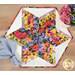 A top down shot of the topper, staged on a wooden table with coordinating flowers and a cloth napkin, complementing the fabrics' vibrant colors and contrasting crisp white fabric..